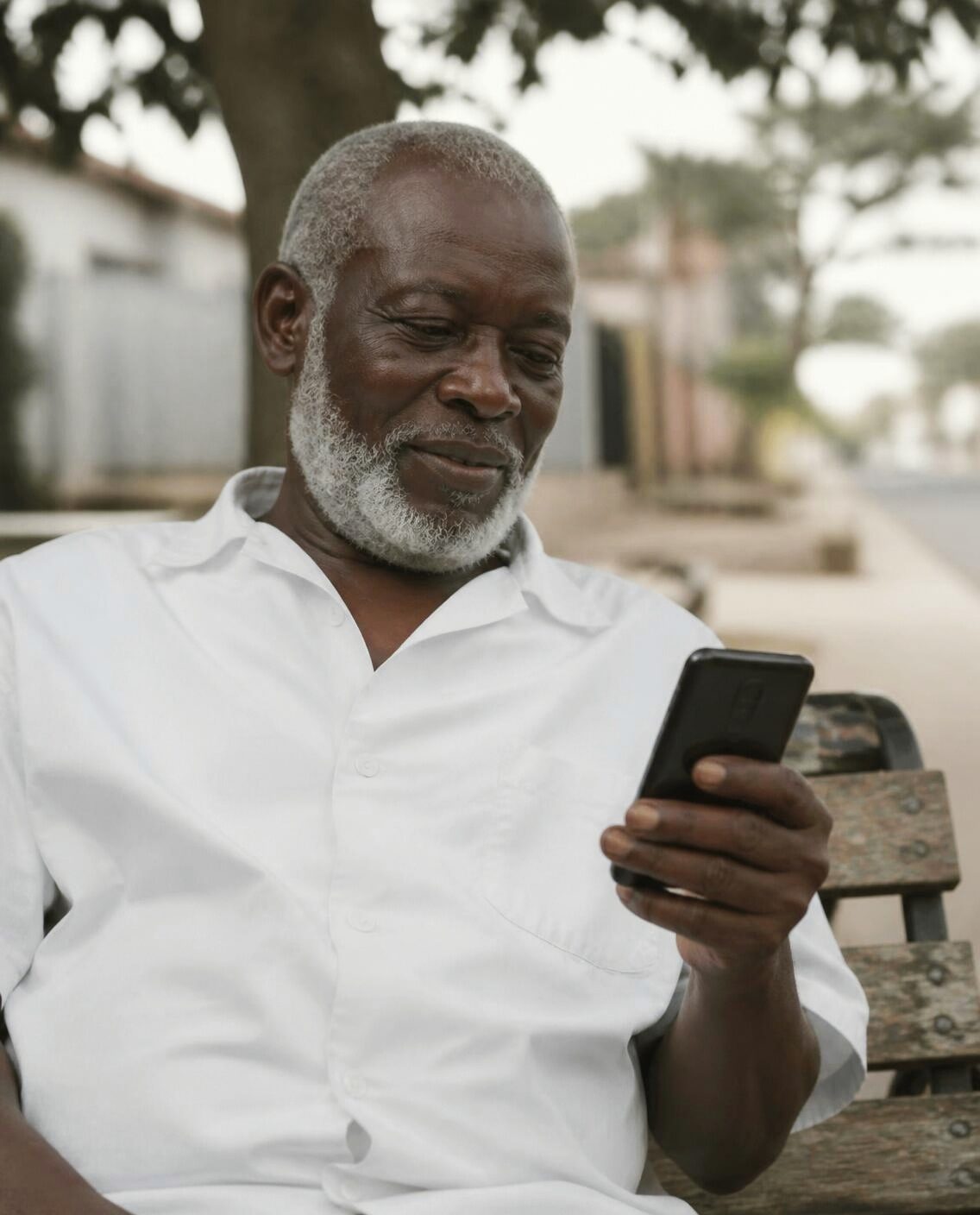 A retired man on a bench, reading a message on his phone.